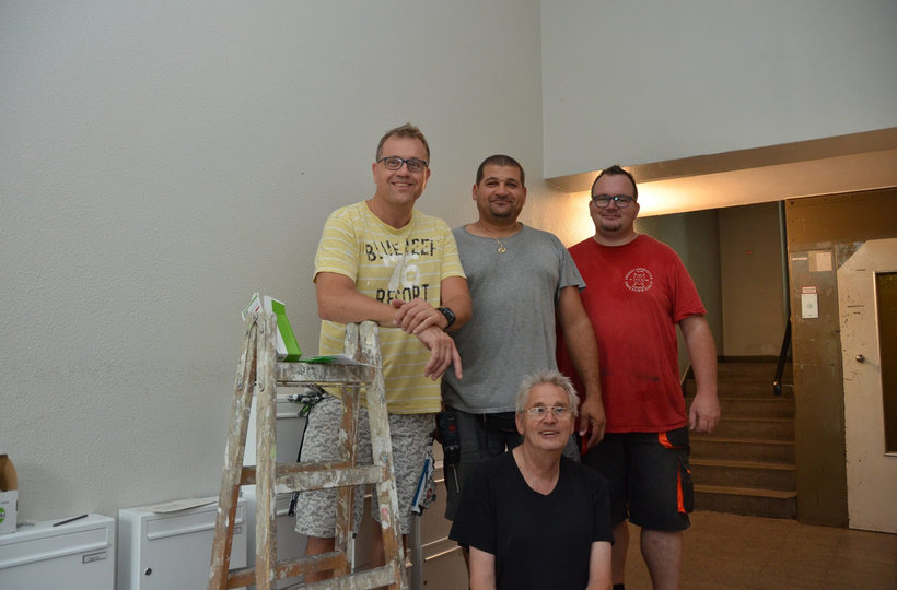 Vier Mitarbeiter des Reparaturmobils stehen in einem Hausflur und lächeln in die Kamera